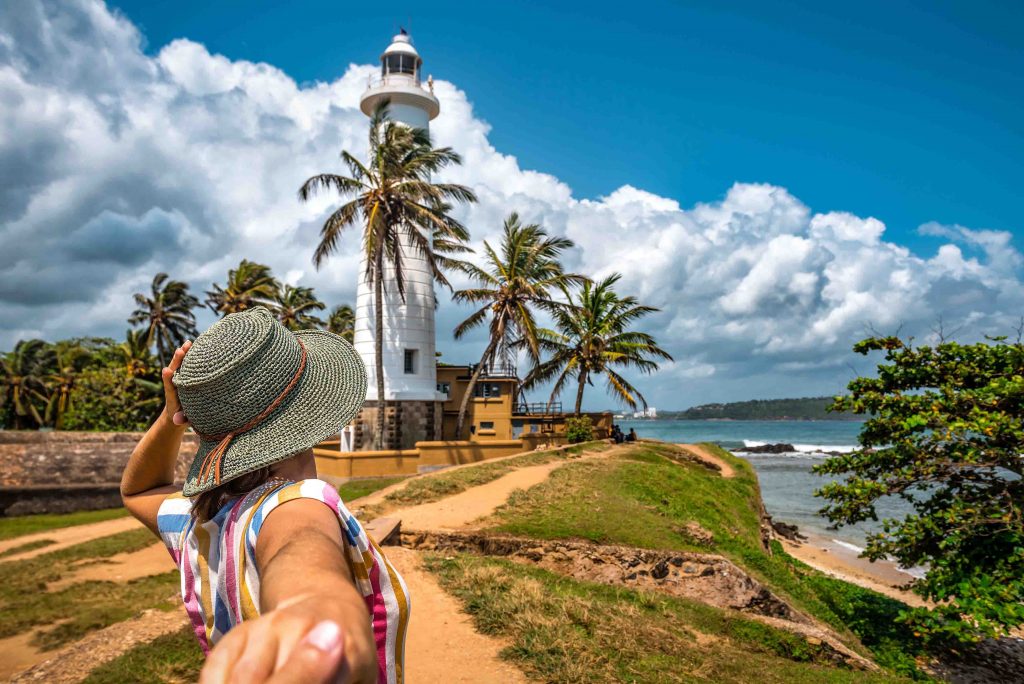 Tourist woman in hat holds man hand an going to the lighthouse on tropical island. Fort Galle. Sri Lanka