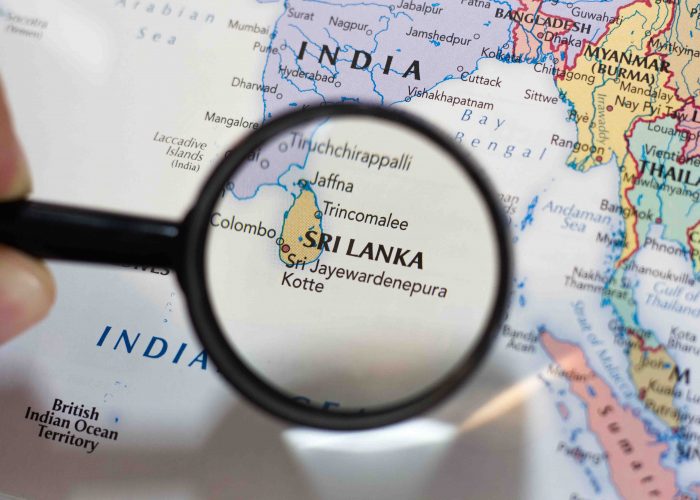 A close-up view of a world map with a magnifying glass highlighting Sri Lanka, the Pearl of the Indian Ocean.