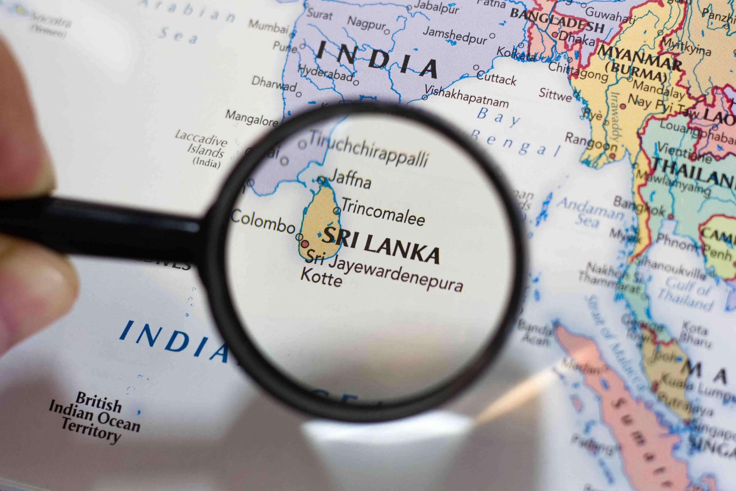 A close-up view of a world map with a magnifying glass highlighting Sri Lanka, the Pearl of the Indian Ocean.